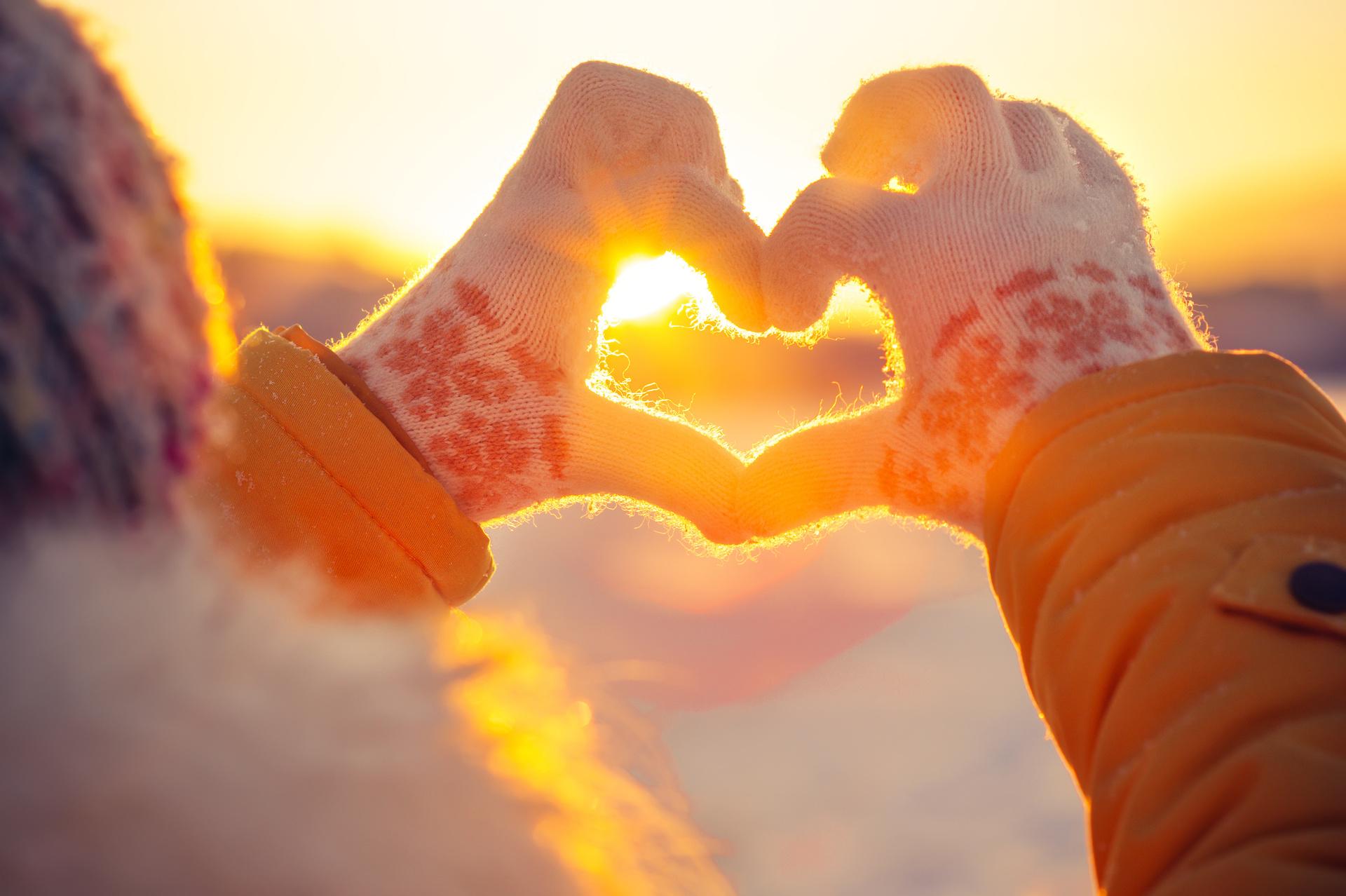 Woman hands in winter gloves Heart symbol with sunset light nature on background