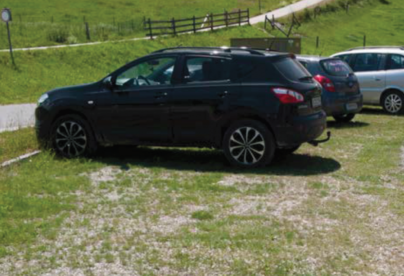 Photograph of cars parked on an area of gravel lawn.