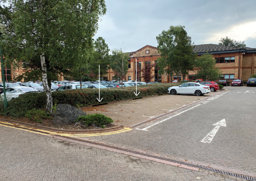 Car park with a central area planted with shrubs and trees between two rows of parking bays. 