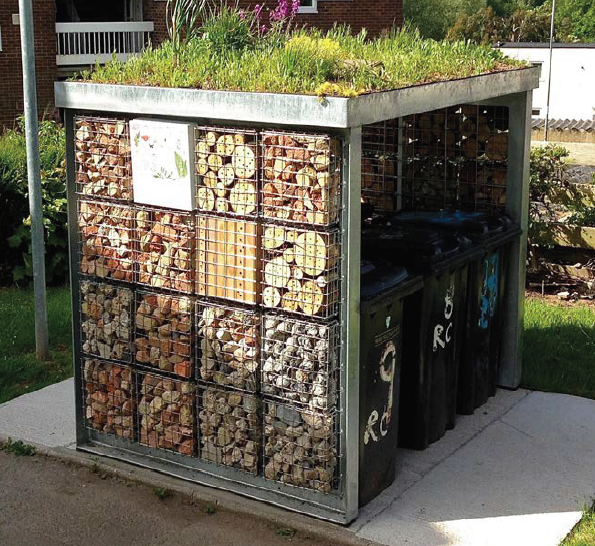 A metal bin shelter with a green roof, with wildlife habitat panels at the sides.