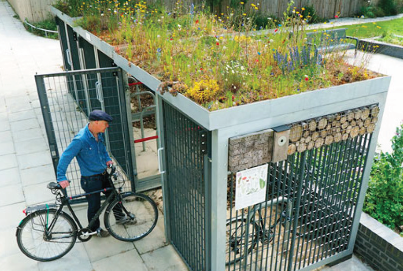 A cyclist putting a bicycle in a cycle shelter with a green roof. 