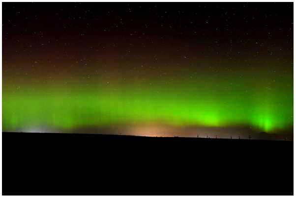 A glowing green sheet of light stretches across the flat horizon with the night sky above