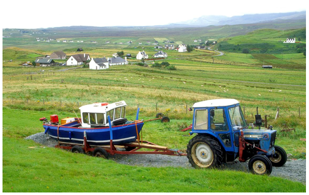 Tractor with boat in the foreground of fields surrounding the small, linear settlement 