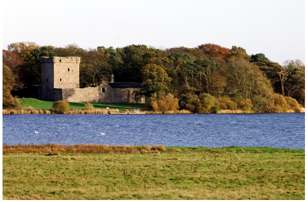 Stone tower and walls visible across the loch surrounded by deciduous woodland.