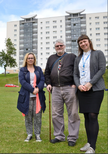three people in greenspace with block of flats behind them