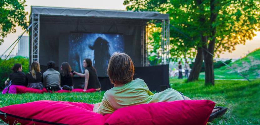 Young people watching an outdoor cinema surrounded by greenery