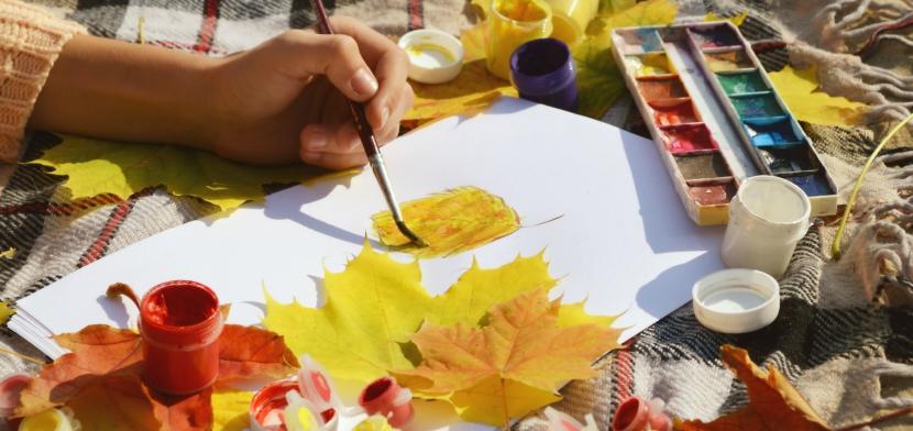 Hand painting on paper surrounded by leaves and paints