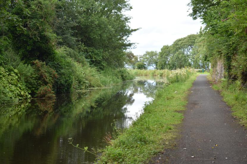 A canal and towpath with trees and greenery on both sides