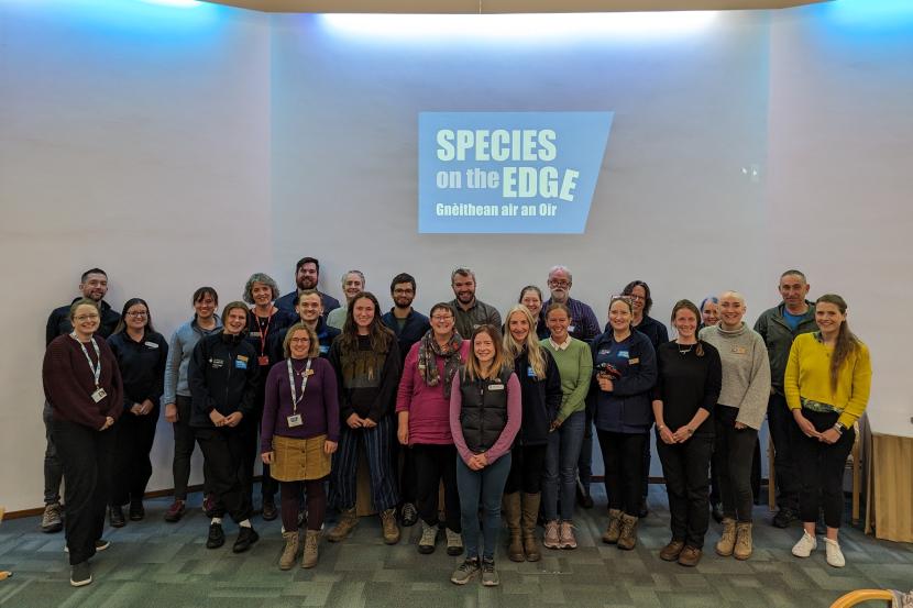 A group photo of the Species on the edge team with their logo on the wall behind them.