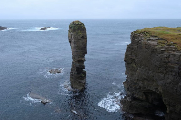 High vertical cliffs with a sea cave at the base and a slim stack to the left.