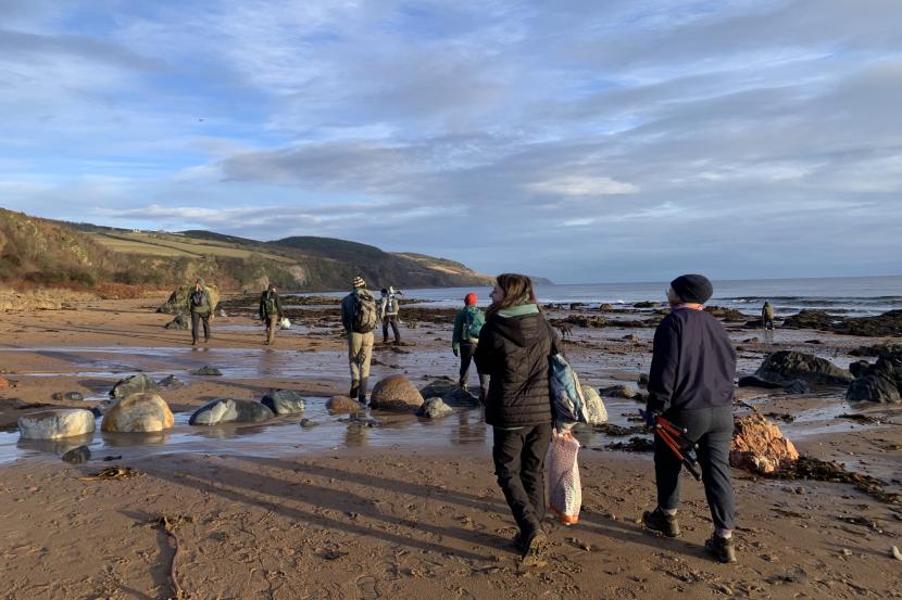 People walking along a beach carrying bags and tools.