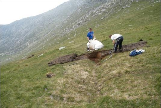 Two men working on a ditch on the side of a hill.