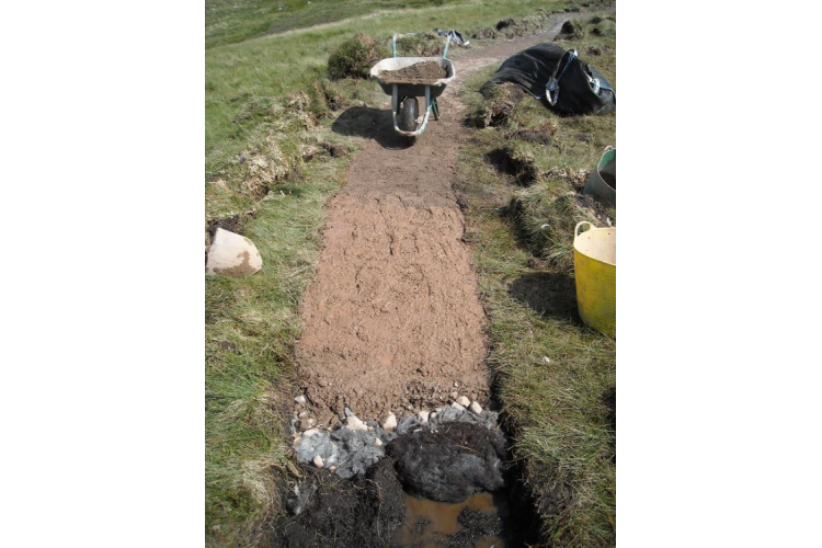 Surfacing added over graded aggregate and sheep fleece to create a cambered path surface slightly above the surrounding ground