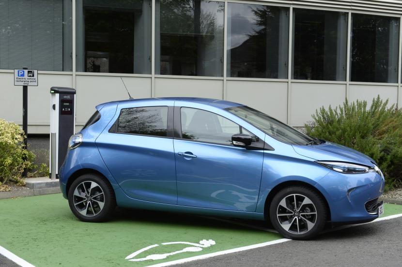An electric car parked at a charging point outside an office building.
