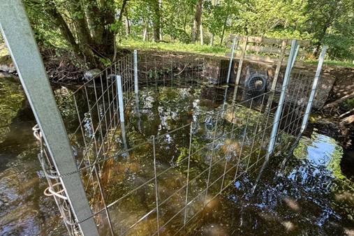 Trapezoidal culvert fence installed in the river beside a riverbank.