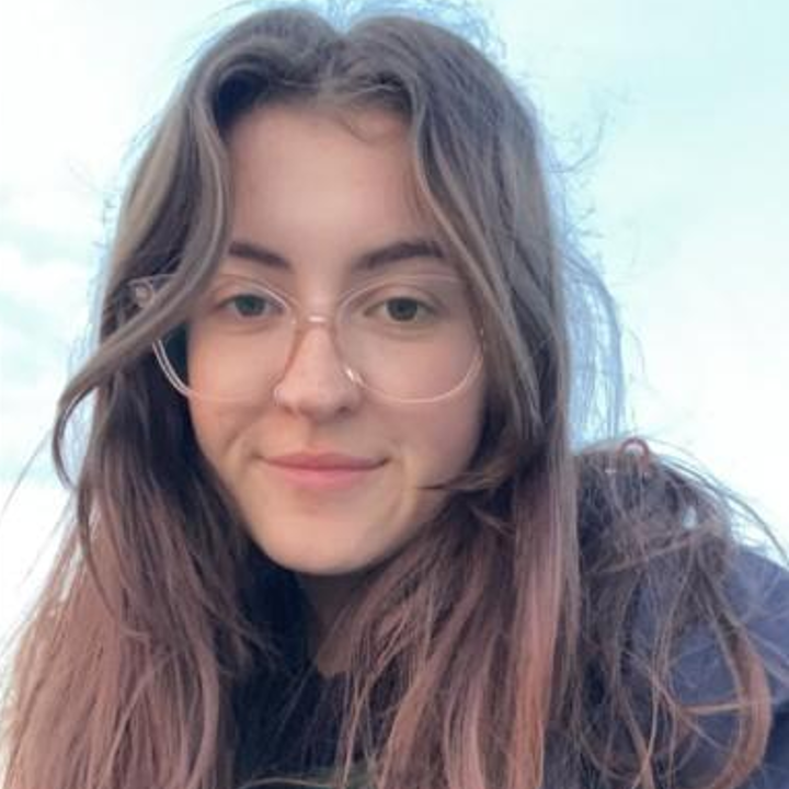 A young woman smiling at the camera with a blue sky in the background.