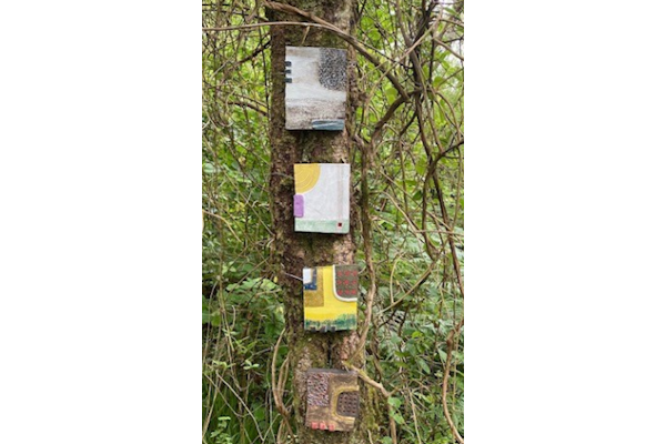 4 ceramic art panels attached to a tree in a woodland