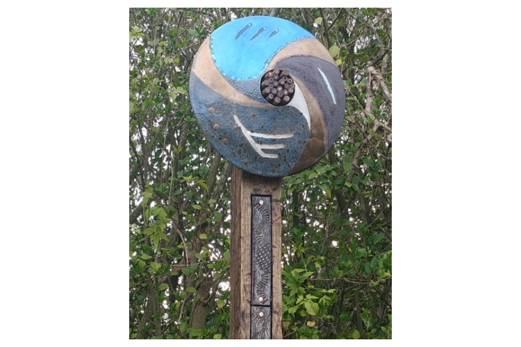 Douglas Kerr art - A post with a metal circle on the top, with wooden straws in the centre hole.