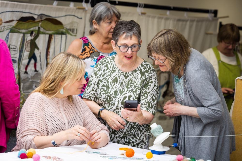 A group of volunteer stitchers surrounding Kirstie Campbell, Spirit of the Highlands &amp; Island tapestry stitch co-ordinator