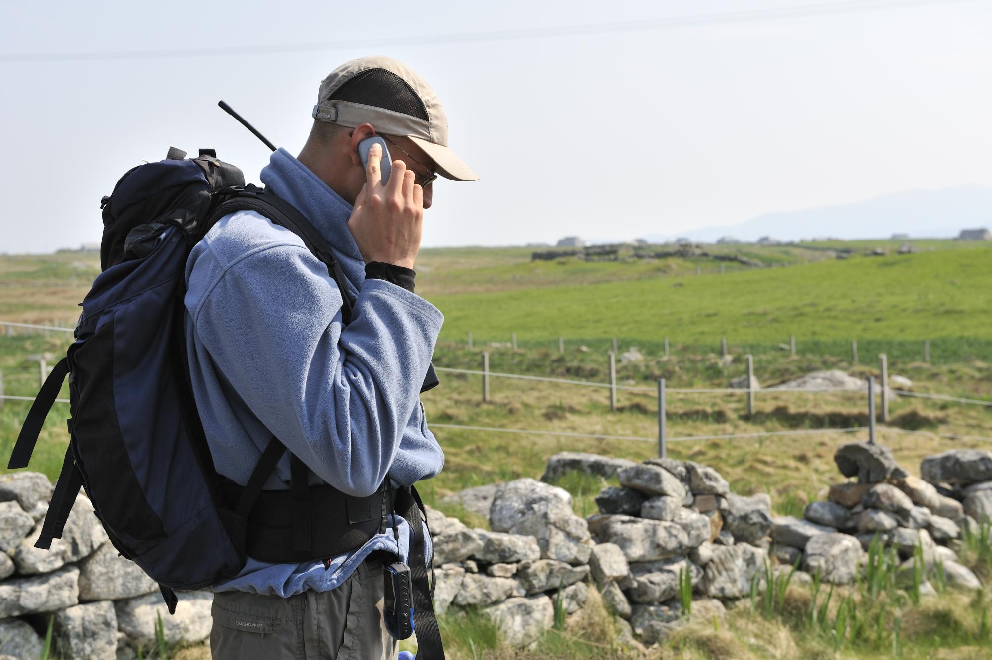 Project officer standing in a field talking on a obile phone.